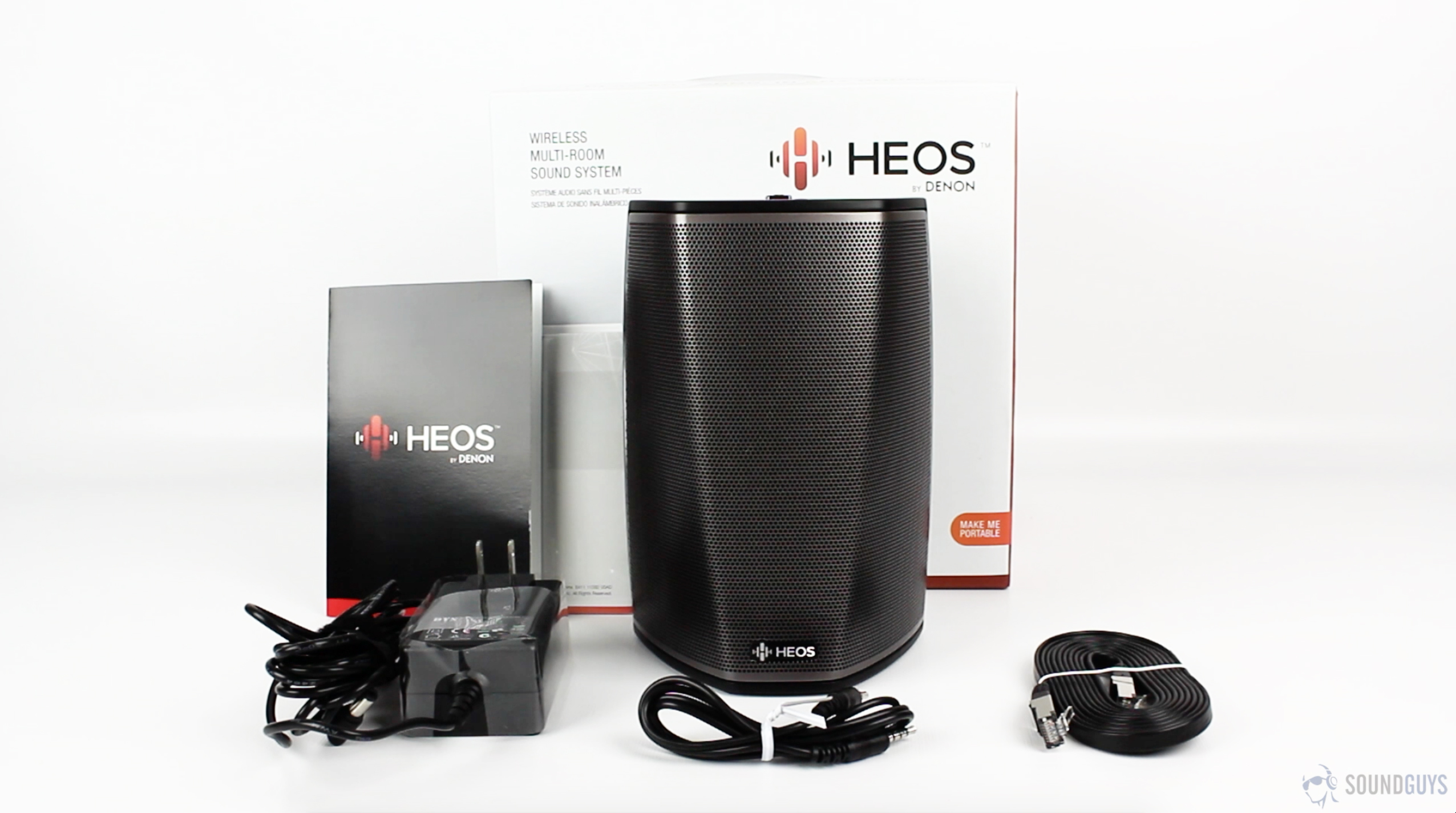 Denon HEOS 1 with box and wires against a white background.