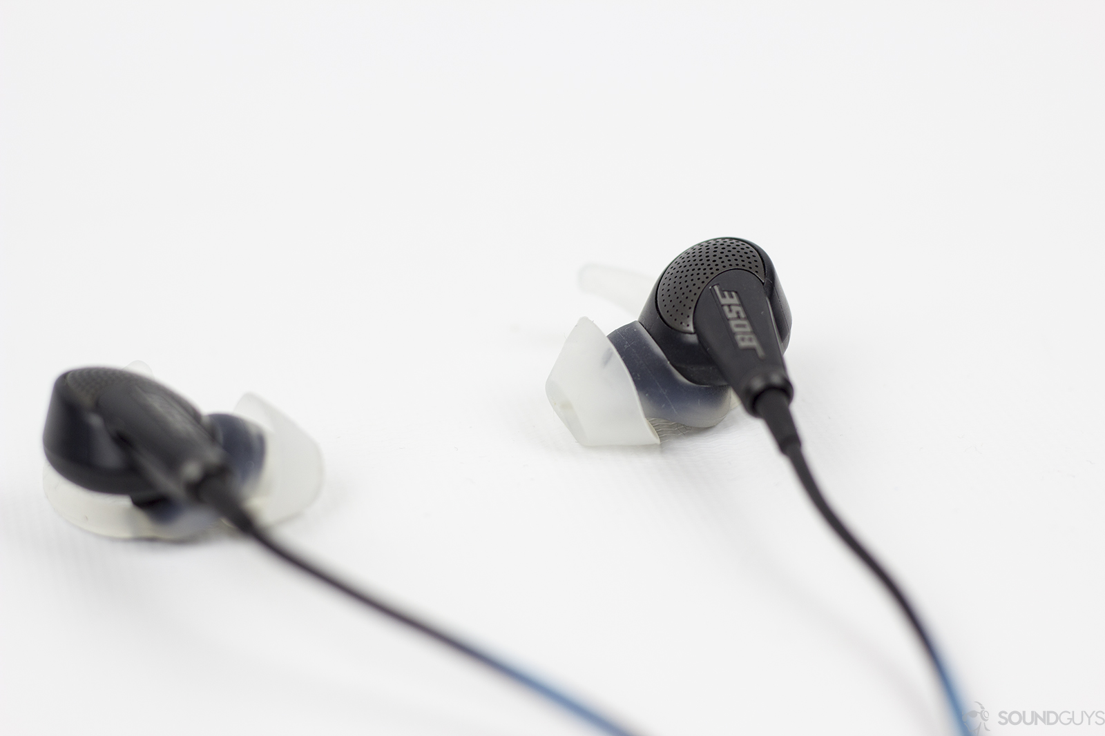 Bose QC 20 noise canceling earbuds on white surface.