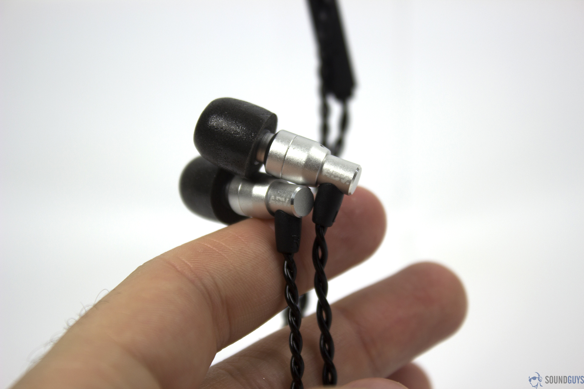 The ADV.SoundM4 earbuds with aluminum housing in the hand on a white backdrop. The ear tips are memory foam.