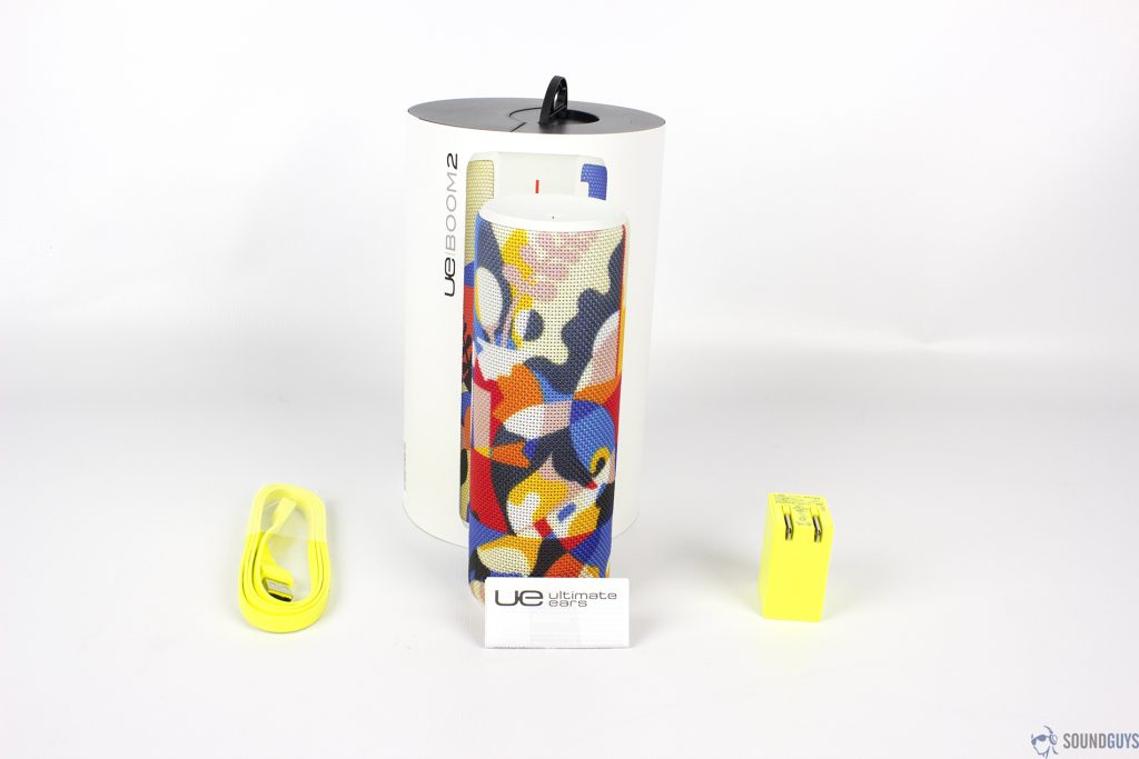The UE Boom 2 packaging along with the bright yellow charging brick and cable on a white background.
