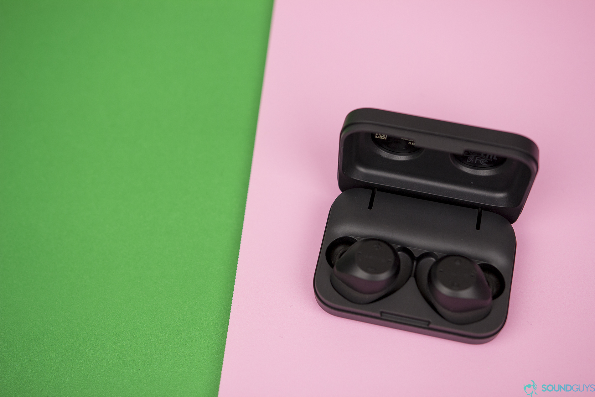 Shot of the open charging case with the Elite Sport true wireless earbuds charging inside against a pink board. 