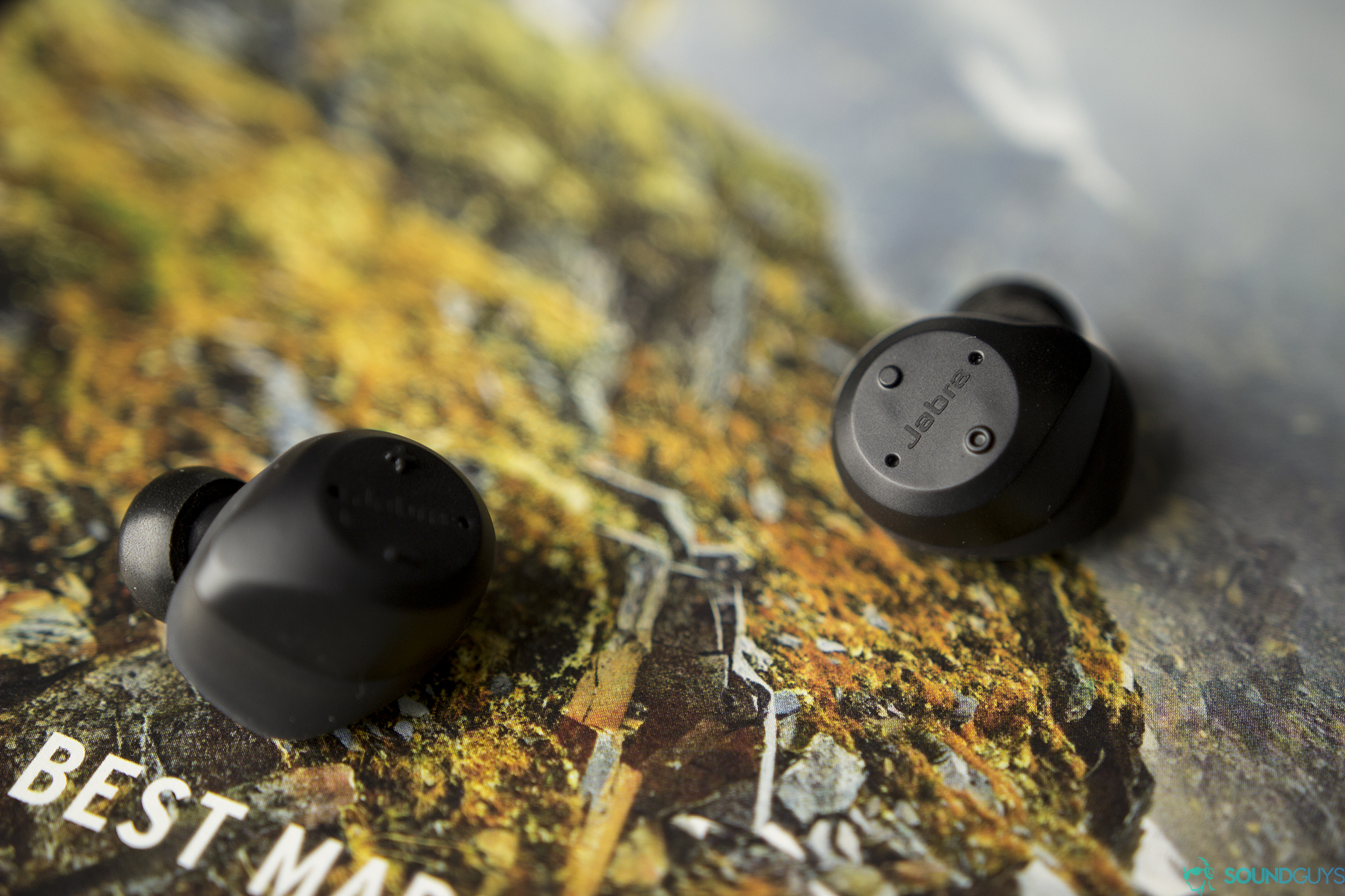 Close-up shot of the playback controls of the Jabra Elite Sport true wireless earbuds on a magazine. 