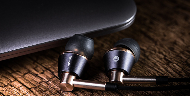The 1MORE triple driver in-ears come in two colorways: silver and gold. Pictured: The 1MORE triple driver in-ear earbuds on a wood surface.