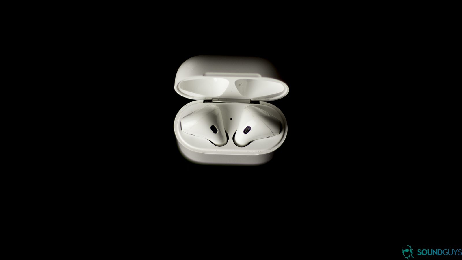The Airpod charging case provides three hours of batter after just 15 minutes of charging. Pictured: A minimalist image with an all black background and an overhead shot of the Apple Airpods placed in the open charging case.