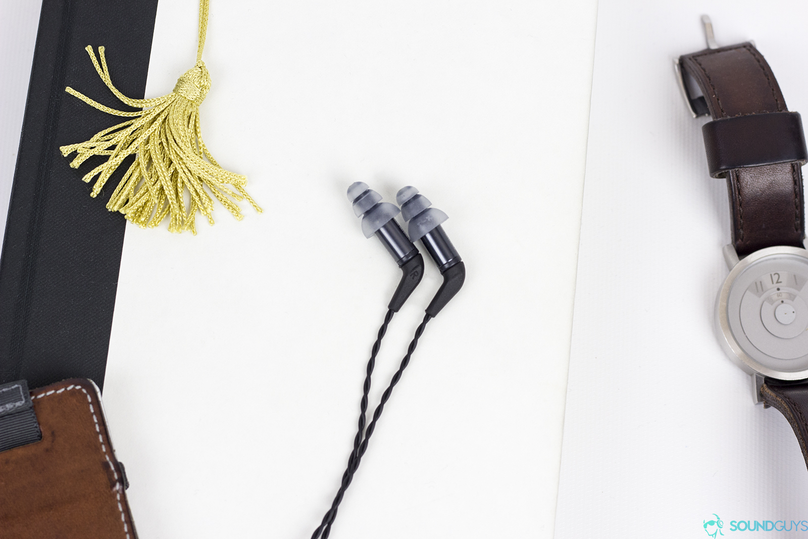 An image of the Eymotic ER4SR in-ears on a white surface next to a bookmark and watch.