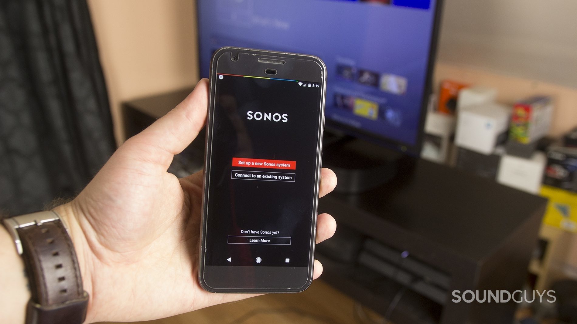 A man holds a phone with the Sonos app in front of the Sonos Playbase.