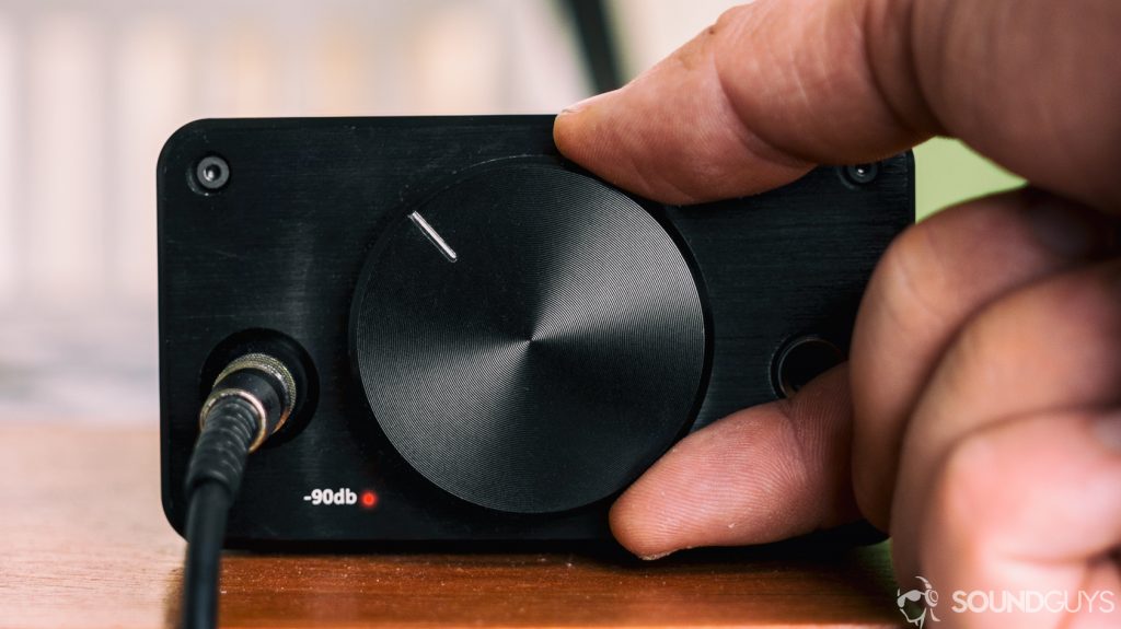 A photo of a hand turning up the knob of a headphone amplifier - dou you need amp for outdoor speakers