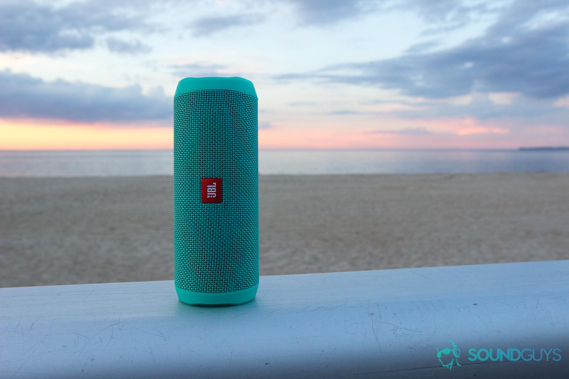 JBL Flip 4 at the beach, with a sunset and the ocean in the background.