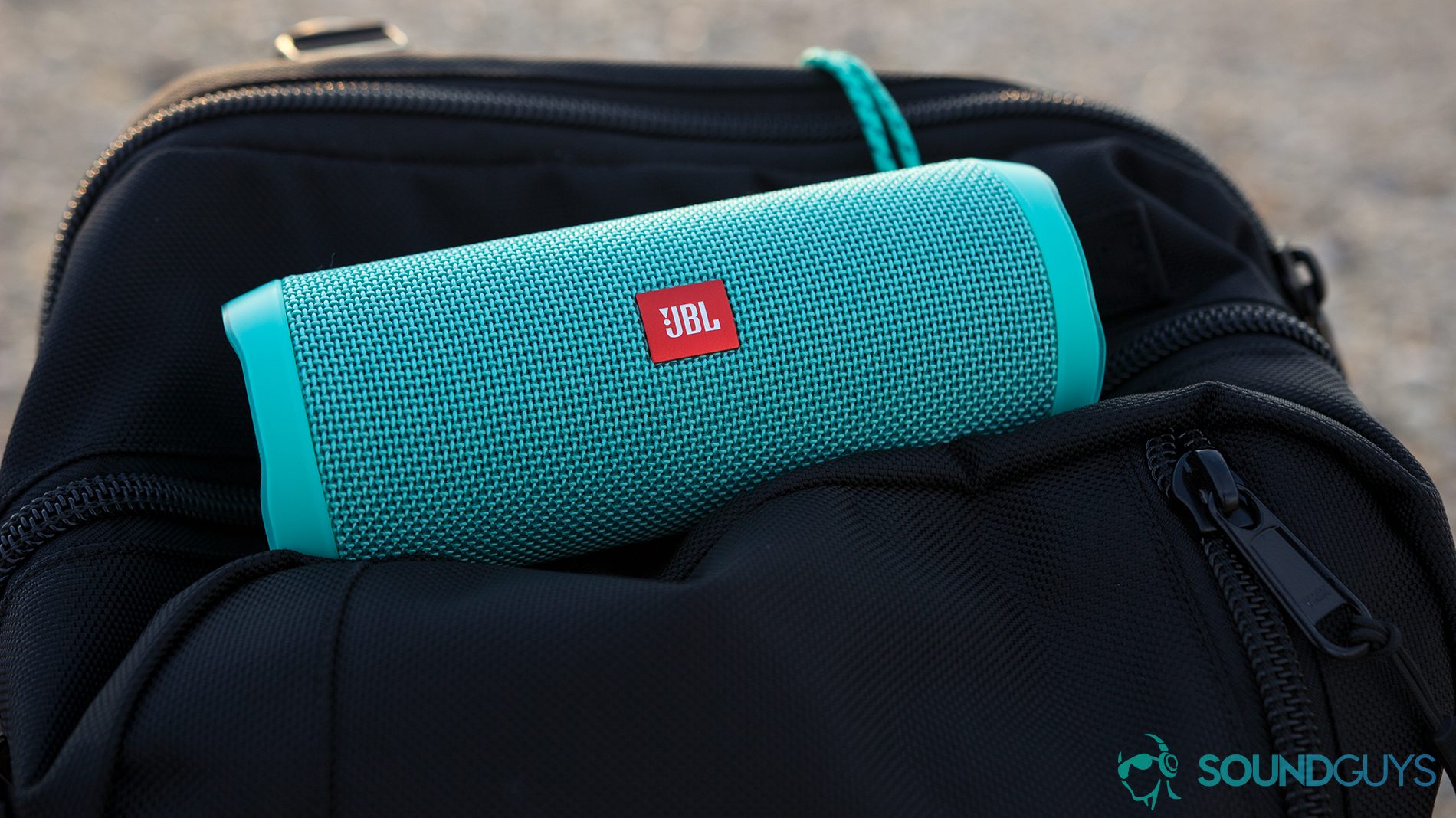 A picture of the JBL Flip 4 waterproof speakers in aqua blue on top of a black backpack.