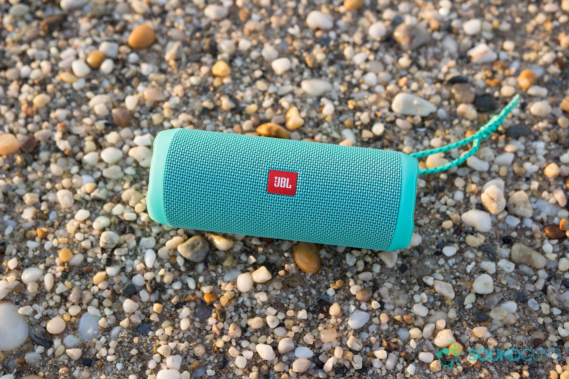 The JBL Flip 4 in teal on a wet pebbled background.