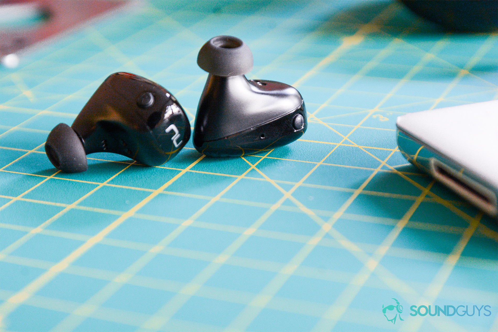 A close-up shot of the Optoma NuForce BE Free8 truly wireless earbuds on a cutting mat.