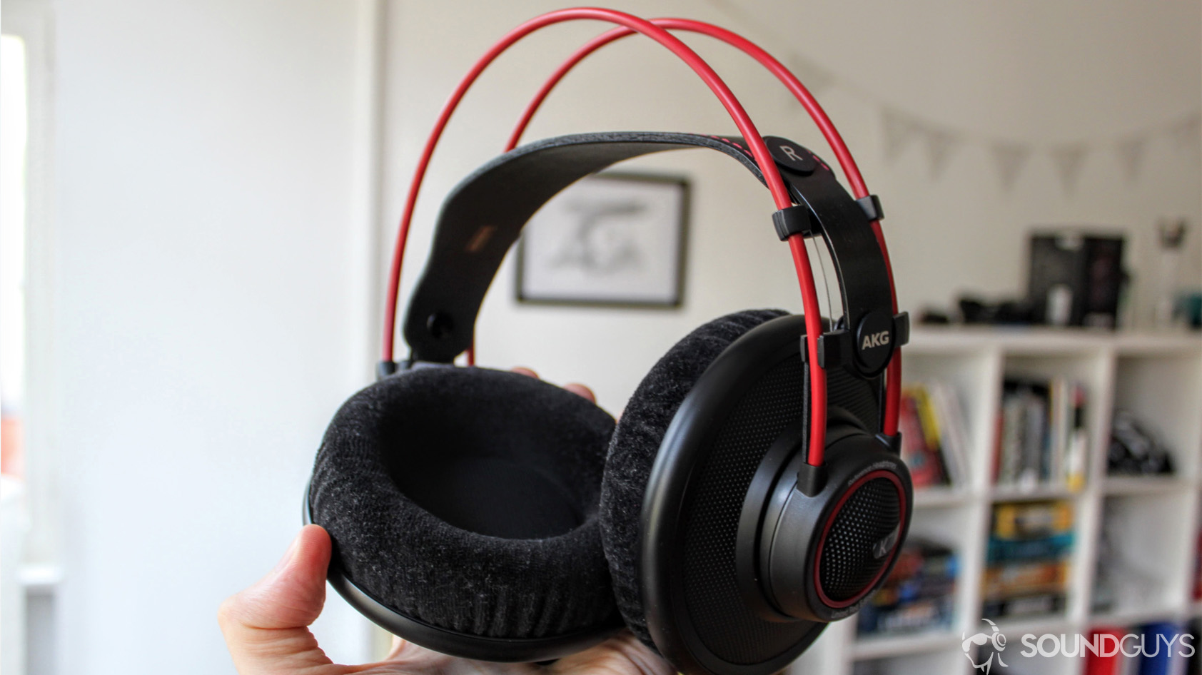 Man holding AKG K7XX's in hand with velour earpads and red frame in focus. 