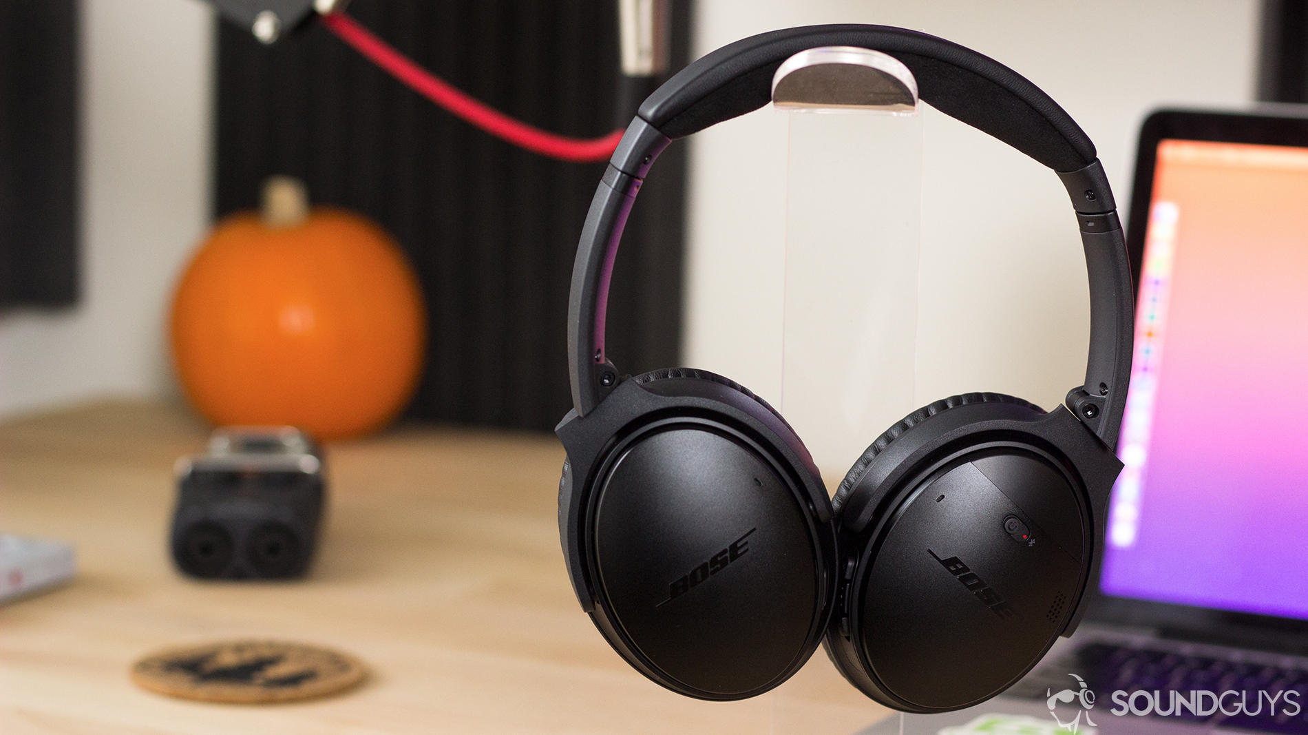 The Bose QuietComfort 35 II headphones on a headphone stand in front of a computer and pumpkin.