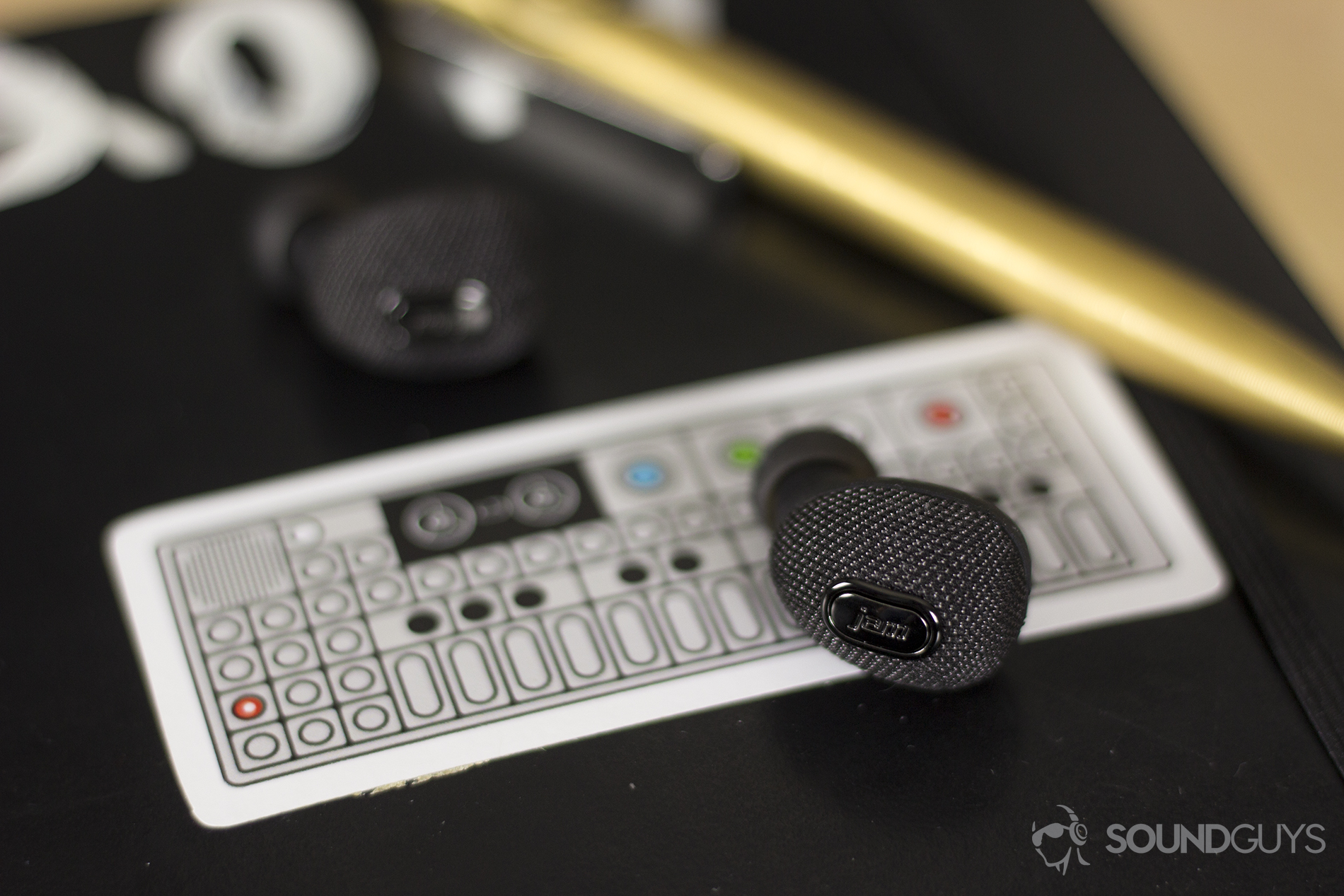 The Jam Ultra earbuds feature one button to control playback. If you want to adjust volume, you'll have to reach for your phone. Pictured: The Jam Ultra earbuds on a sticker for a backdrop. In the background is a gold pen on a black surface.