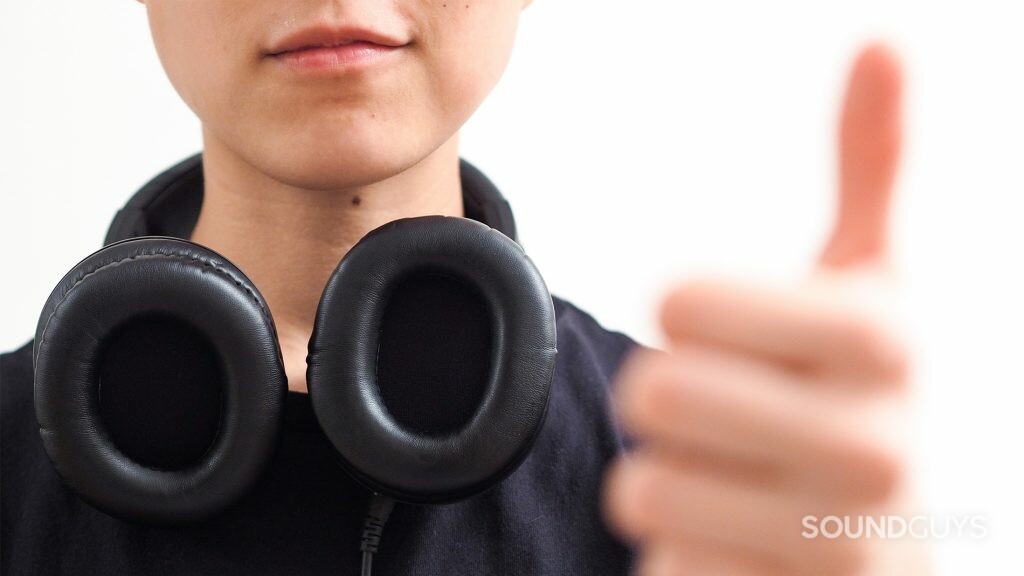 Best headphones under $100: The headphones flat on the chest while being worn around the neck. There is a thumbs up on the right side of the image.