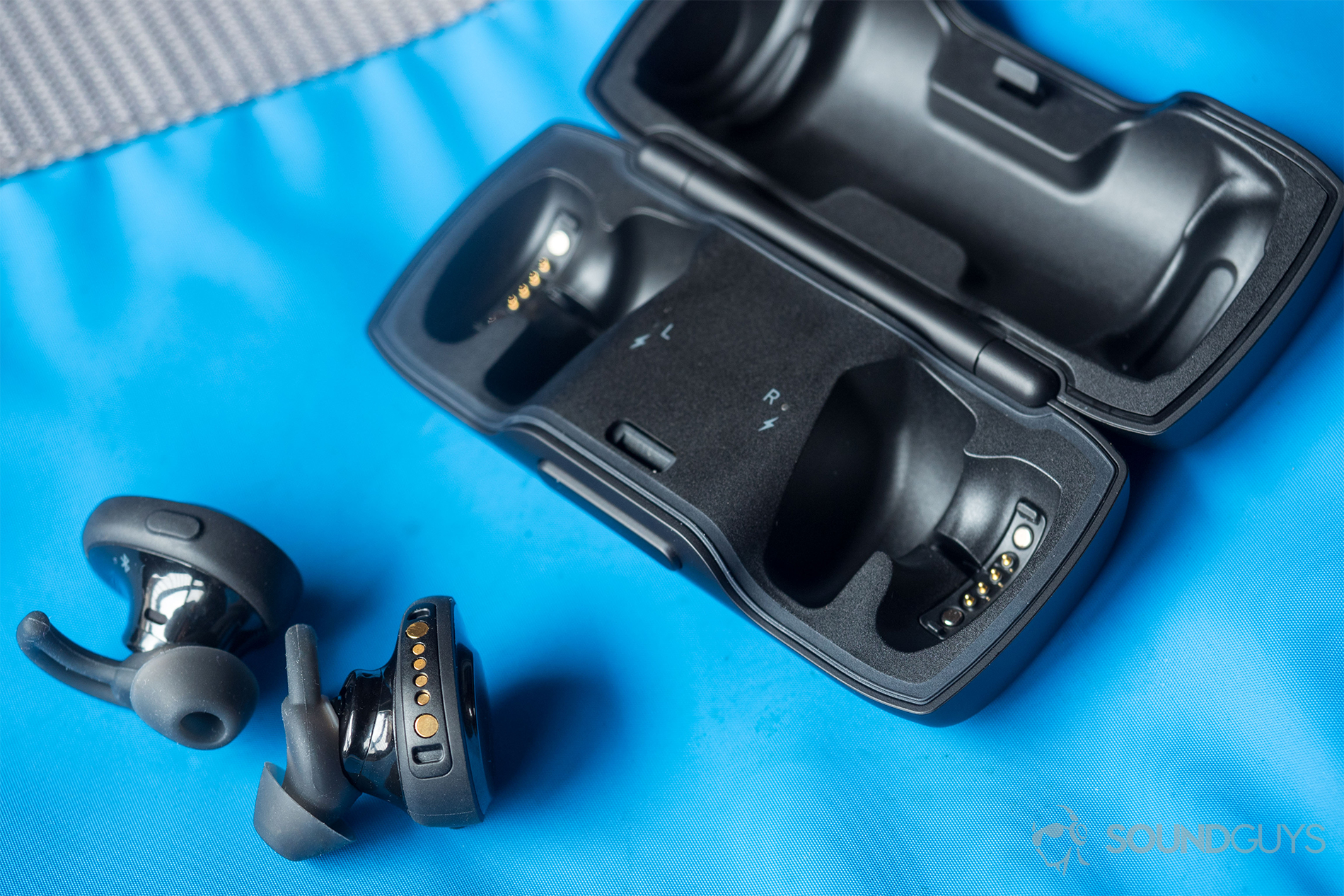 A photo of the Bose SoundSport Free true wireless workout earbuds outside of the open charging case on top of a blue surface.