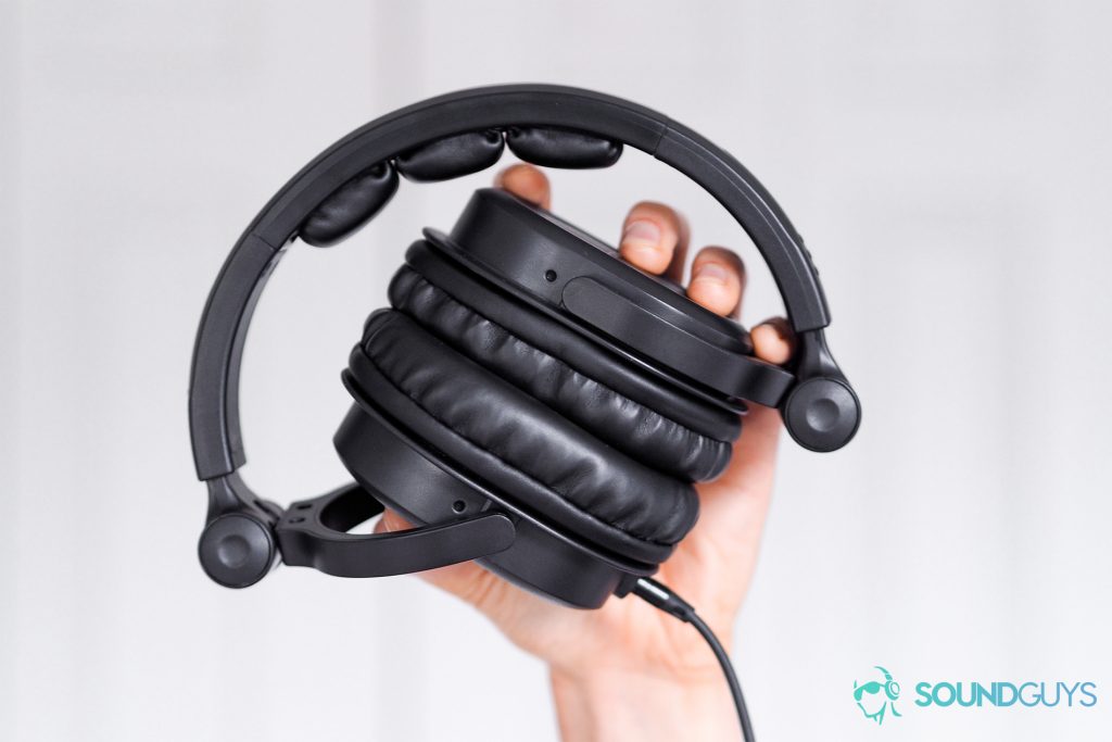 Best headphones under $200: The Monoprice 8323 over-ear headphones being raised in a hand. White background.
