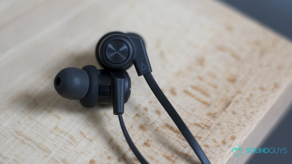 Creative Outlier One: Earbuds stacked on top of each other on wood surface.
