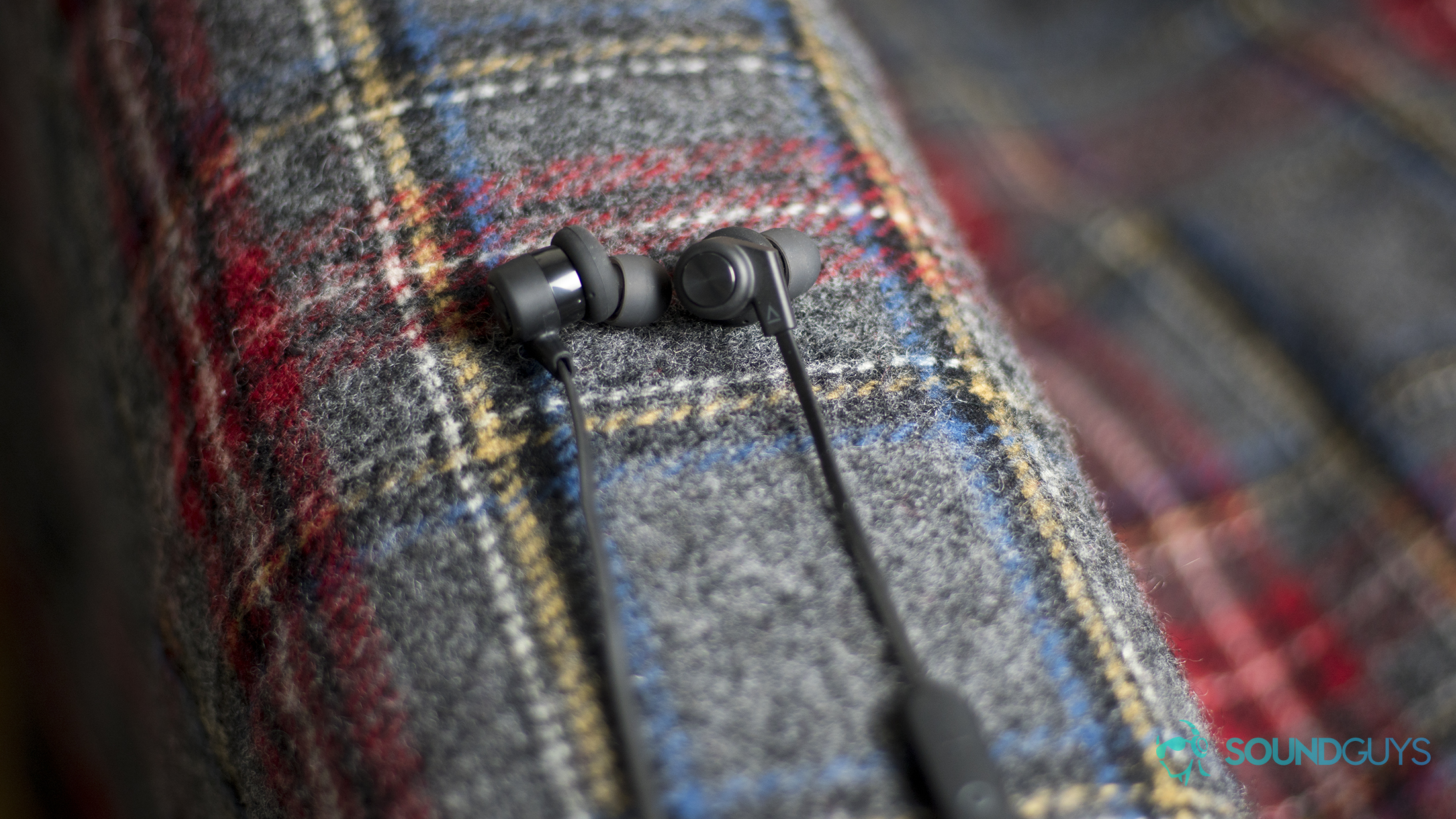 Creative Outlier One: Earbuds resting flat on a plaid surface.