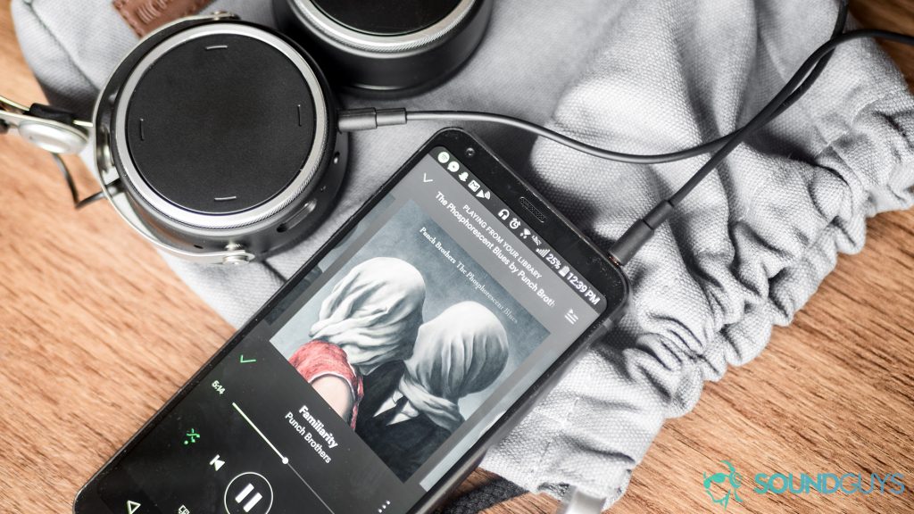 Best headphones under $100: The Beyerdynamic Aventho Wireless headphones are in the top left corner of hte image to show both ear cups, the right of which is a touch-control panel. On the bottom of the screen is an LG G6 with spotify pulled up, revealing the Punch Brothers' album artwork for the Phosporescent Blues. The items are on top of the included padded, canvas carrying pouch.