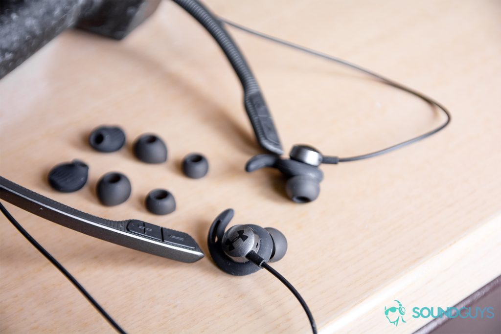 Under Armour Sport Flex Wireless by JBL headphones on a wood surface with ear and wing tips.