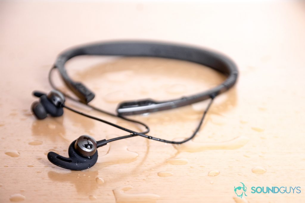 Under Armour Sport Flex Wireless by JBL image of the earbuds surrounded by water droplets on wood surface.