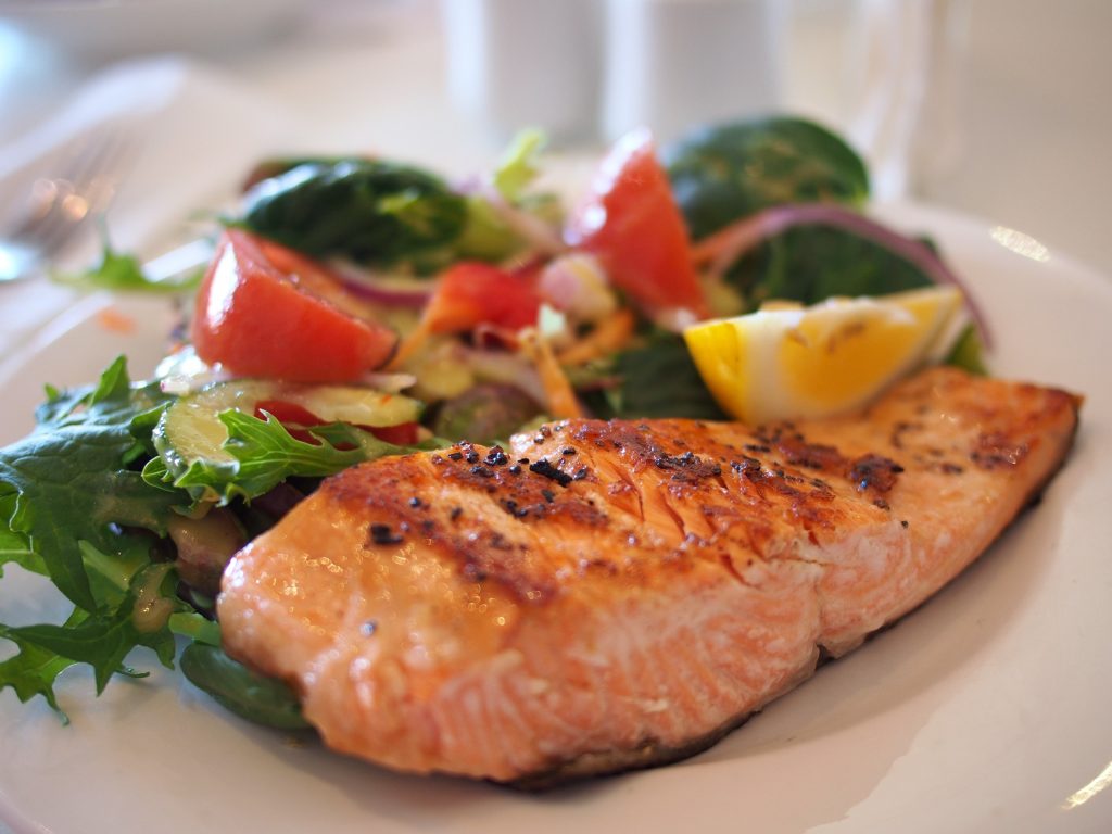 A photo of a Salmon dinner with salad and lemon.
