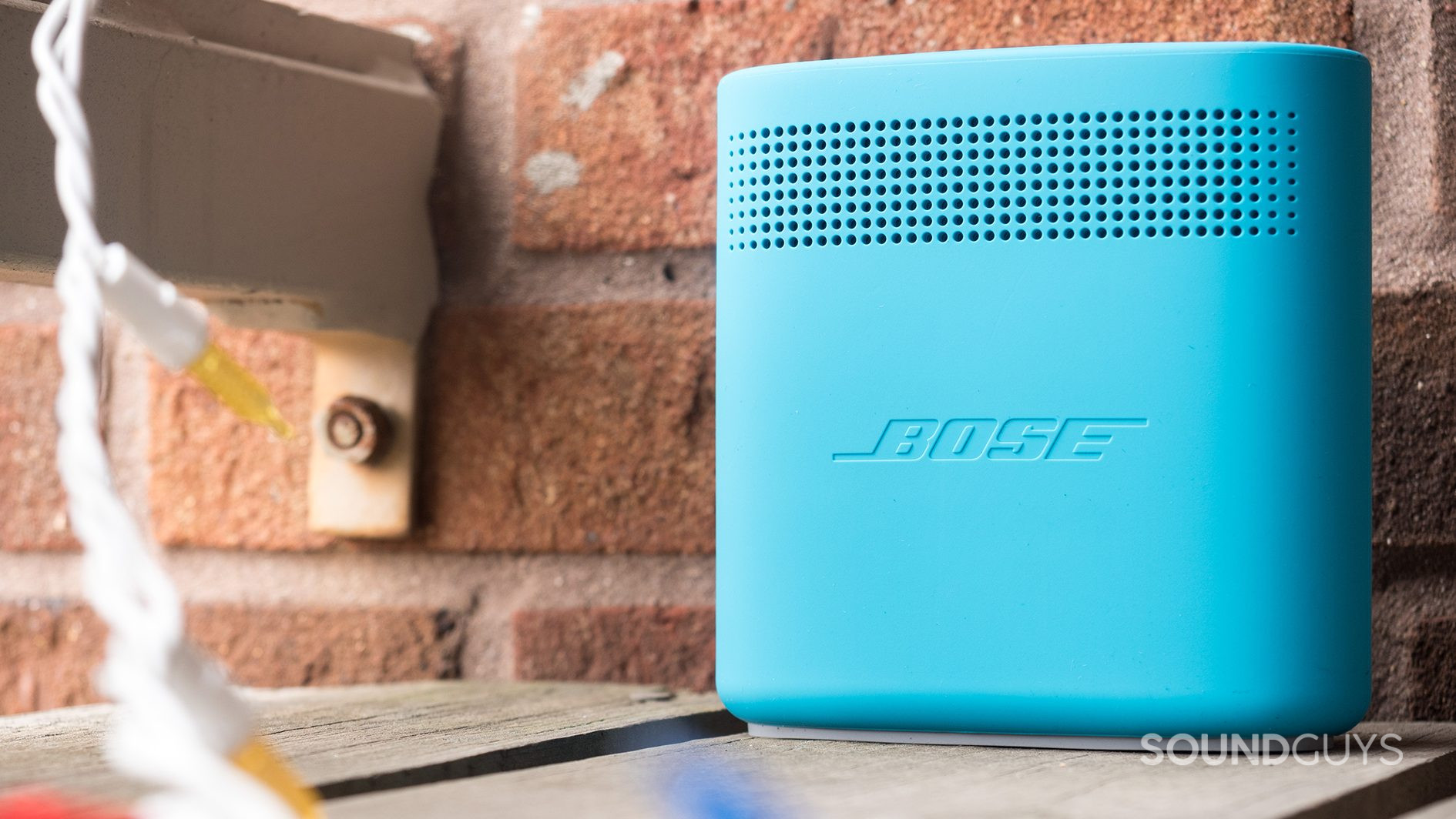 The Bose SoundLink Color II in blue on a wooden porch against a brick background.