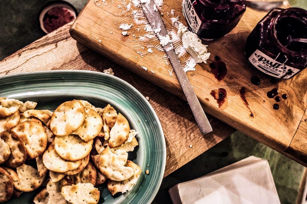 A photo of crackers, blueberry jam, and chevre goat cheese on a wooden cutting board.