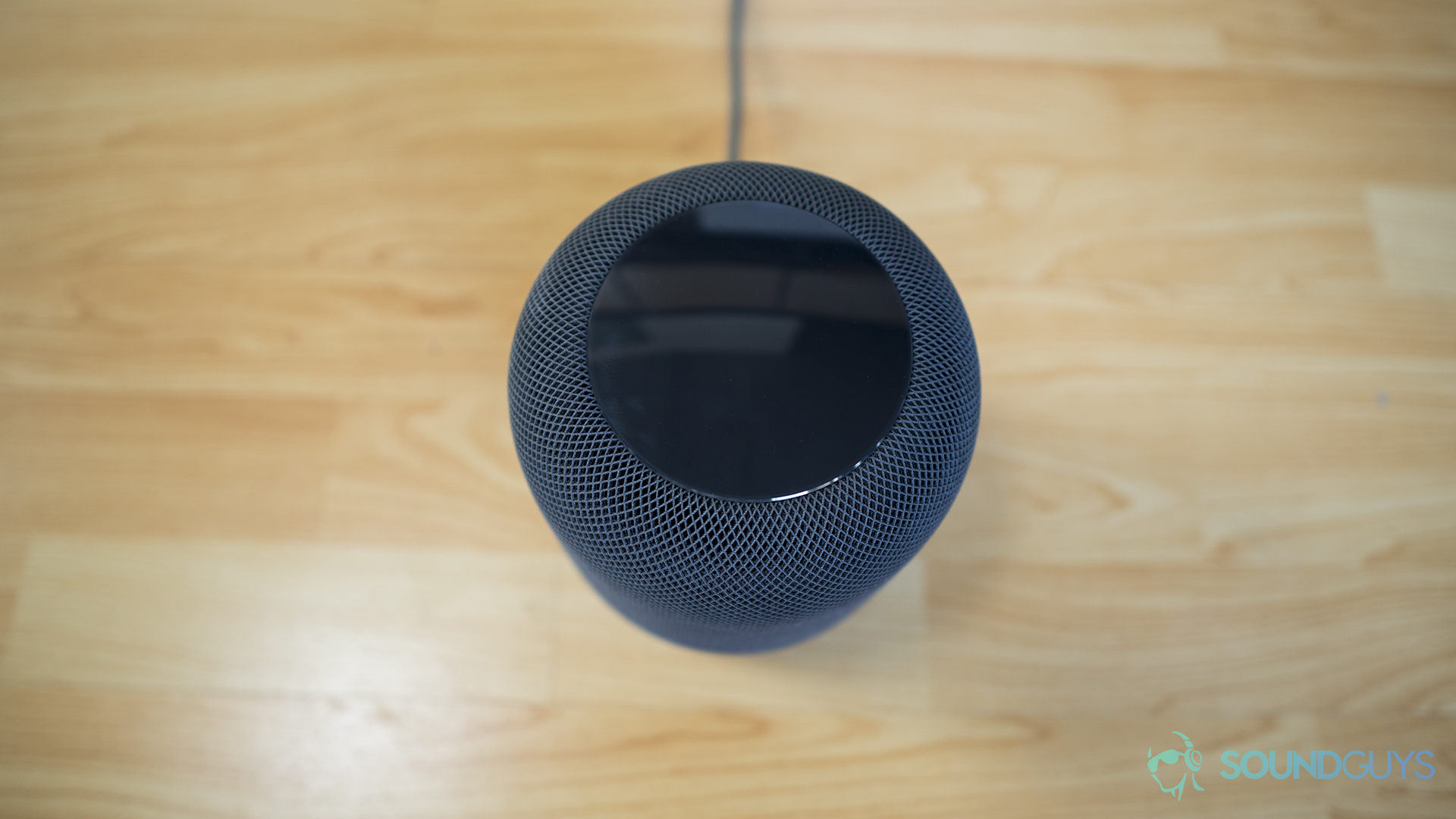 A photo of an Apple HomePod sitting on a wooden table.