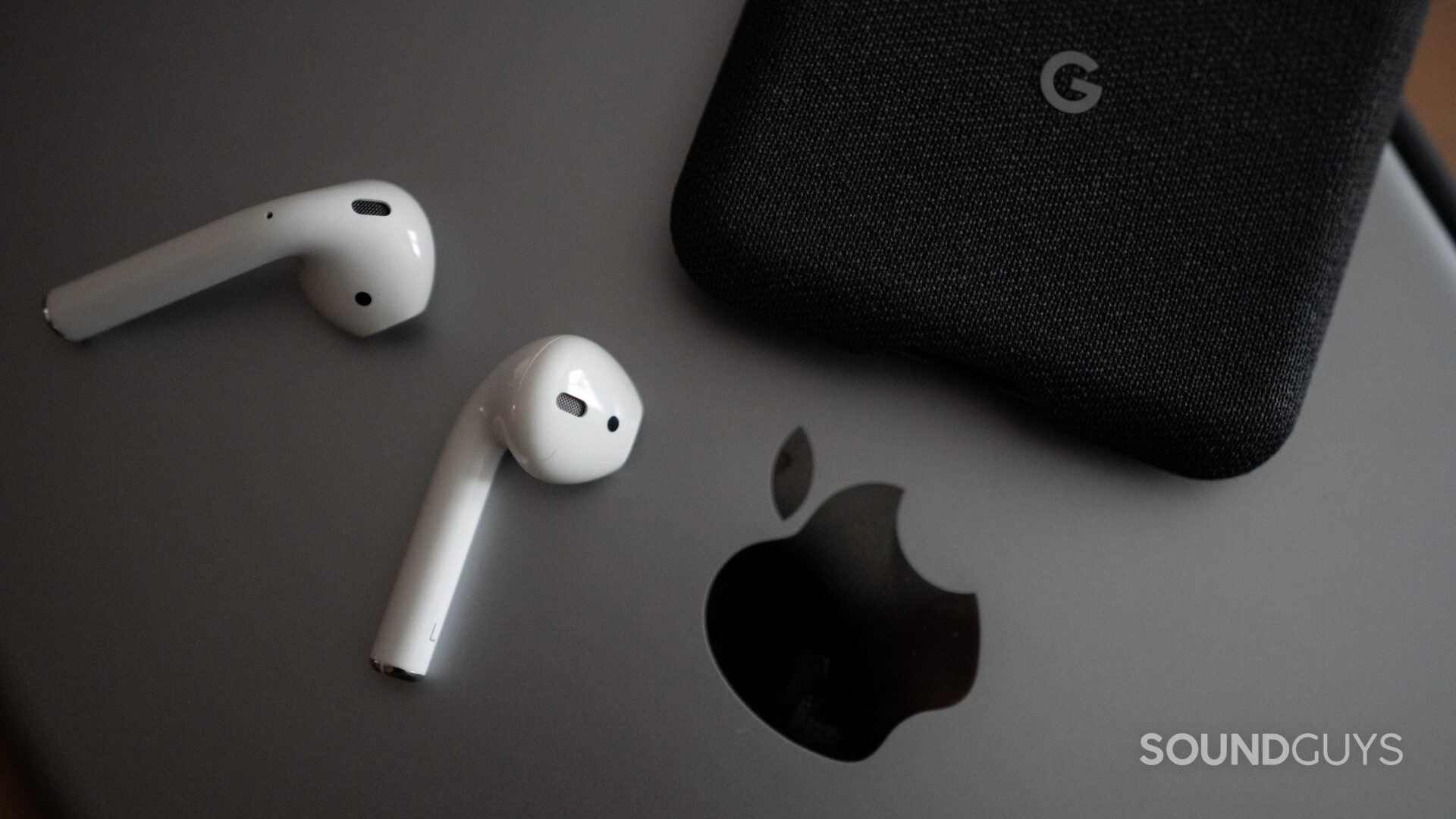 The AirPods (2nd generation) on top of an iPad and next to the Google Pixel 3.