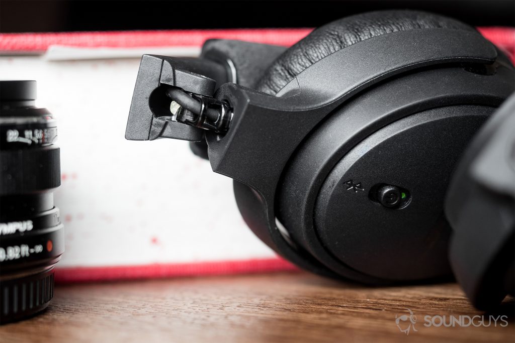 The right ear cup of the Bose On-Ear Wireless flipped inward to reveal superglue within the hinge. To the left is a partially visible black Olympus lens with a closed dictionary as a backdrop.