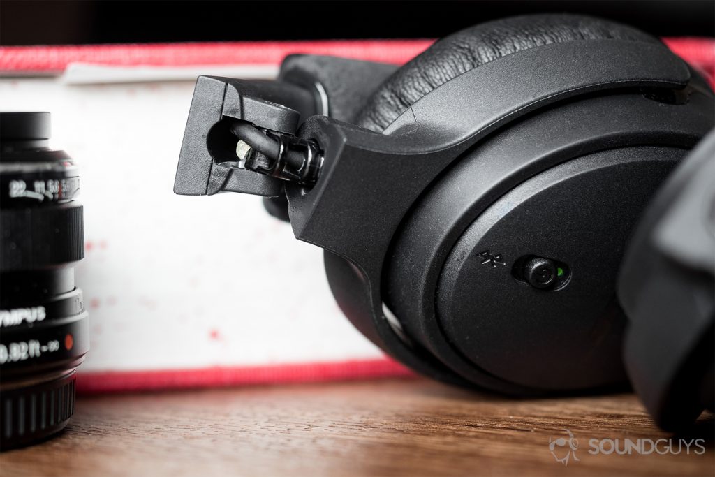 On the right side of our Bose On-Ear Wireless unit, there is visible superglue in the right hinge, making me question the construction quality that much more. Pictured: The right ear cup of the Bose On-Ear Wireless flipped inward to reveal superglue within the hinge. To the left is a partially visible black Olympus lens with a closed dictionary as a backdrop.