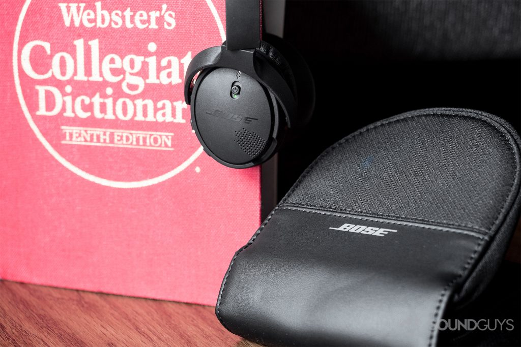 The included carrying case is reminiscent of CD carrying cases. Though the retro styling may be polarizing, it's compact shape is appreciated when using a bag with limited real-estate. Pictured: The Bose On-Ear Wireless draped over a red dictionary, and the included D-shaped zipper protective case is next to it.