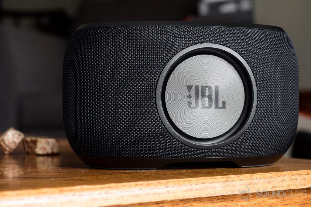 JBL Link 300 Google Assistant-integrated smart speaker: The speaker is rear-facing to show off the passive radiator, branded with the JBL logo. The speaker is black.