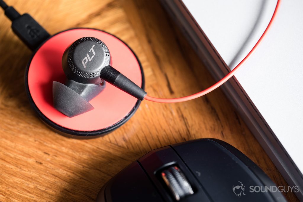 Finding the right ear tips: In typical Plantronics-style, the Voyager 6200 UC maintain a stable connection with ease. Class 1 Bluetooth allows for users to travel up to 30 meters from the source. Pictured: The earbud placed on the reverse side of the charging cradle. The bottom of it matches the orange/poppy-red accents of the headset. In the bottom-left corner of the photo is the top-third of a Logitec Anywhere MX mouse, and a Microsoft Surface Book takes up the upper-right, diagonal third of the photo.