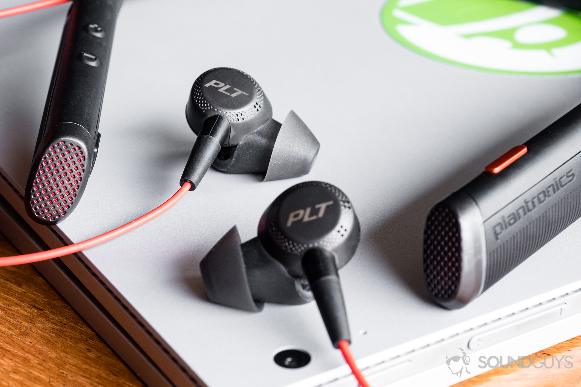 As one may expect, the Plantronics Voyager 6200 UC earphones favor vocal-heavy music. Bass reproduction is the weakest aspect of the earphones' sound. Pictured: The Plantronics Voyager 6200 UC on top of a Microsoft Surface Book. The lower-left and right diagonal sections are a wood table, and the headset rests atop the laptop with teh earbuds between the ends of the neckband.