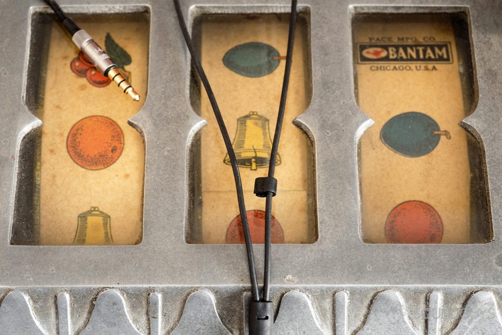 Above the Y-splitter of the RHA MA650 is a rubber piece that zips the separated cables together to prevent them from getting caught on objects. Pictured: The cable of the RHA MA650 earphones and 3.5mm headphone jack on top of a slot machine.