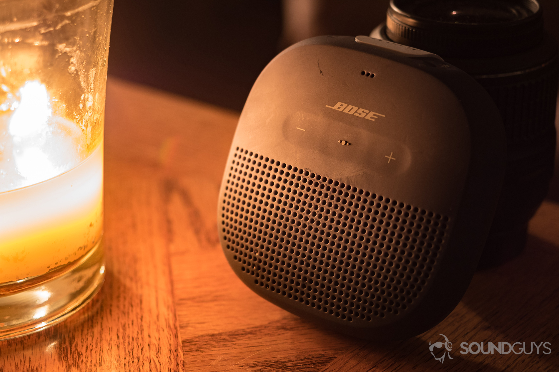 The Bose SoundLink Micro (blue) next to a large candle on a wood tabletop.