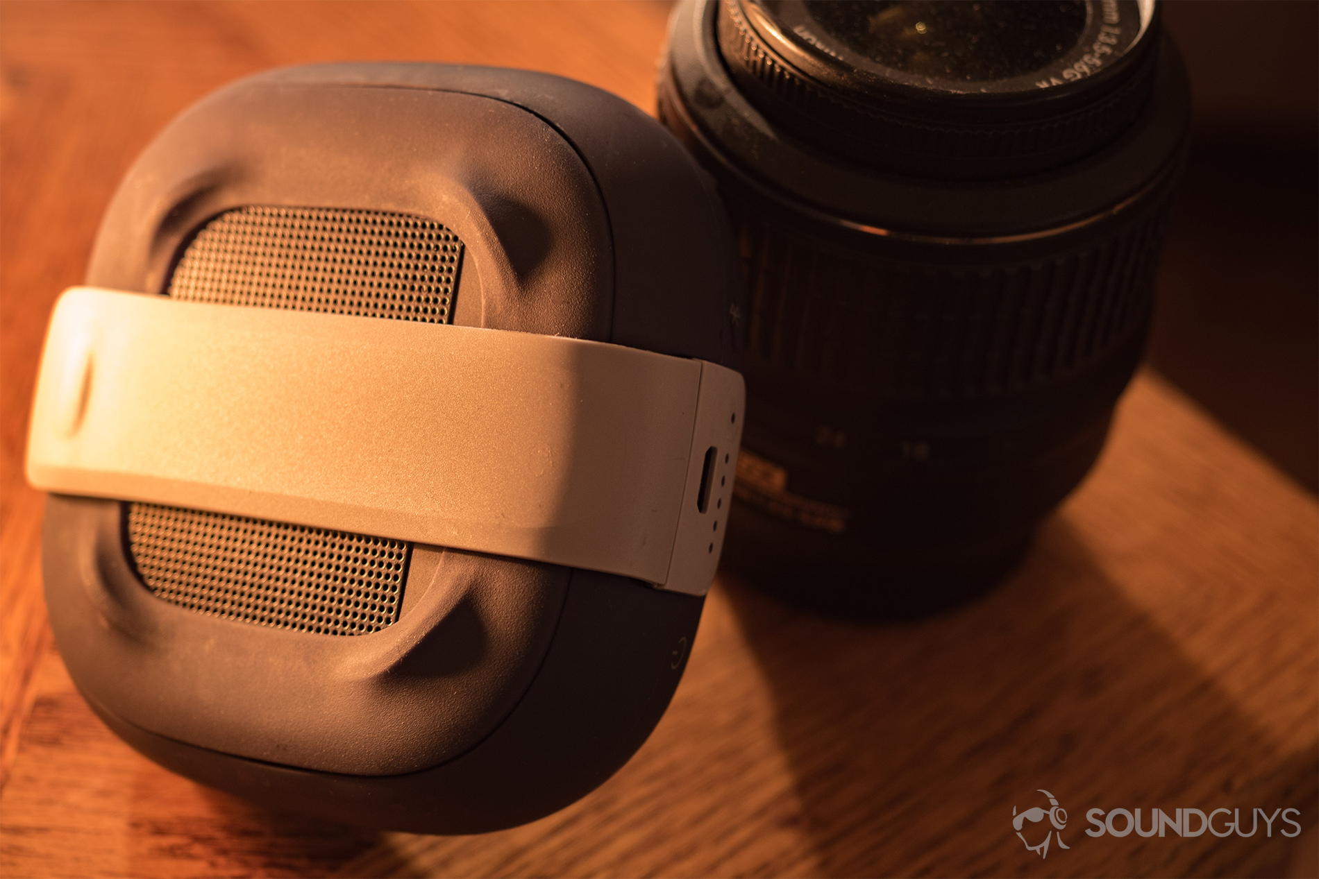 The Bose SoundLink Micro (blue) leaning against a Nikon kit lens in candle light.