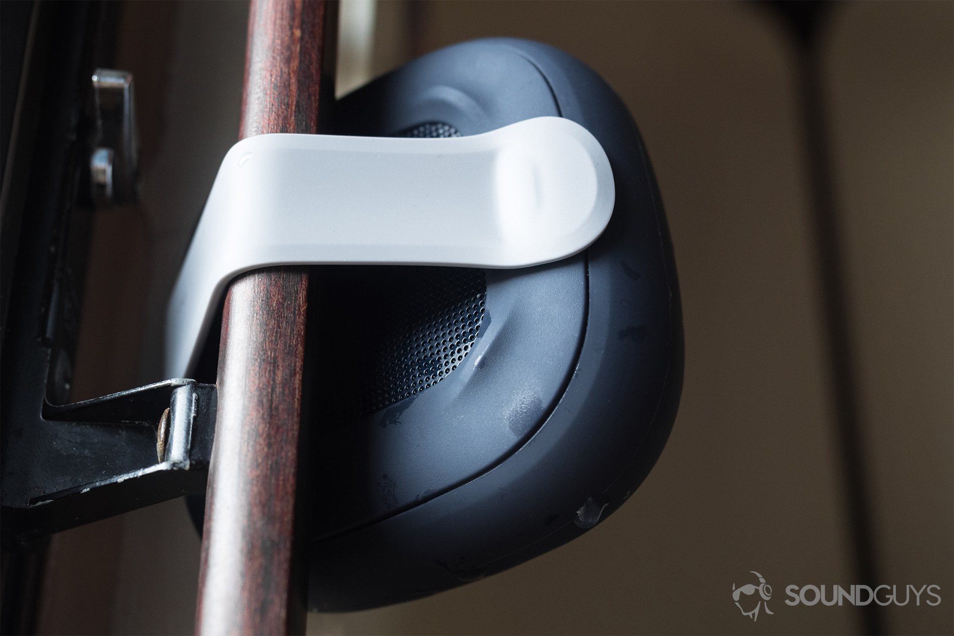 The Bose SoundLink Micro (blue) hooked around a sliding door handle. It's a rear, up-facing photo.