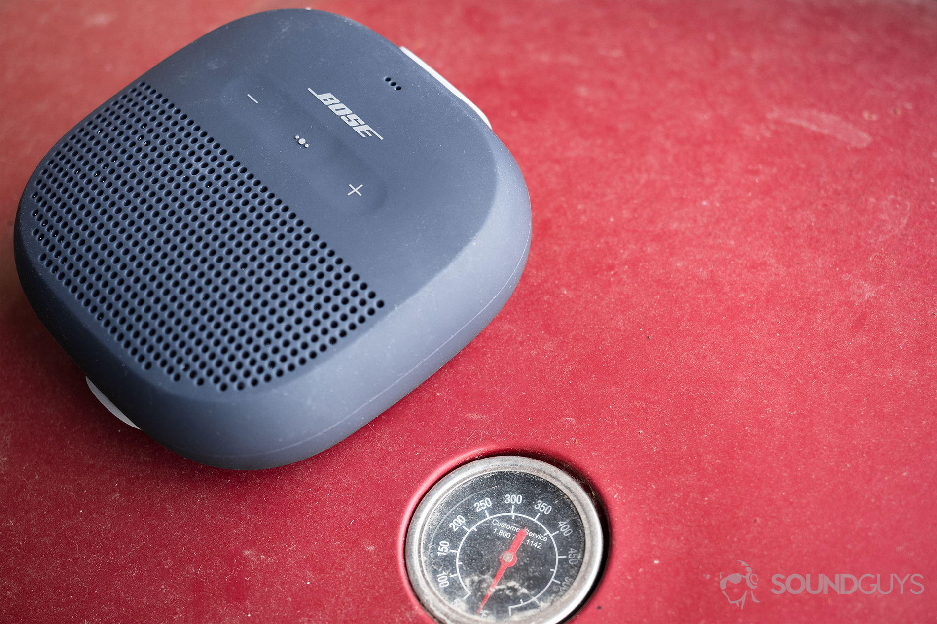 Bose SoundLink Micro on a red grill with the thermometer showing.