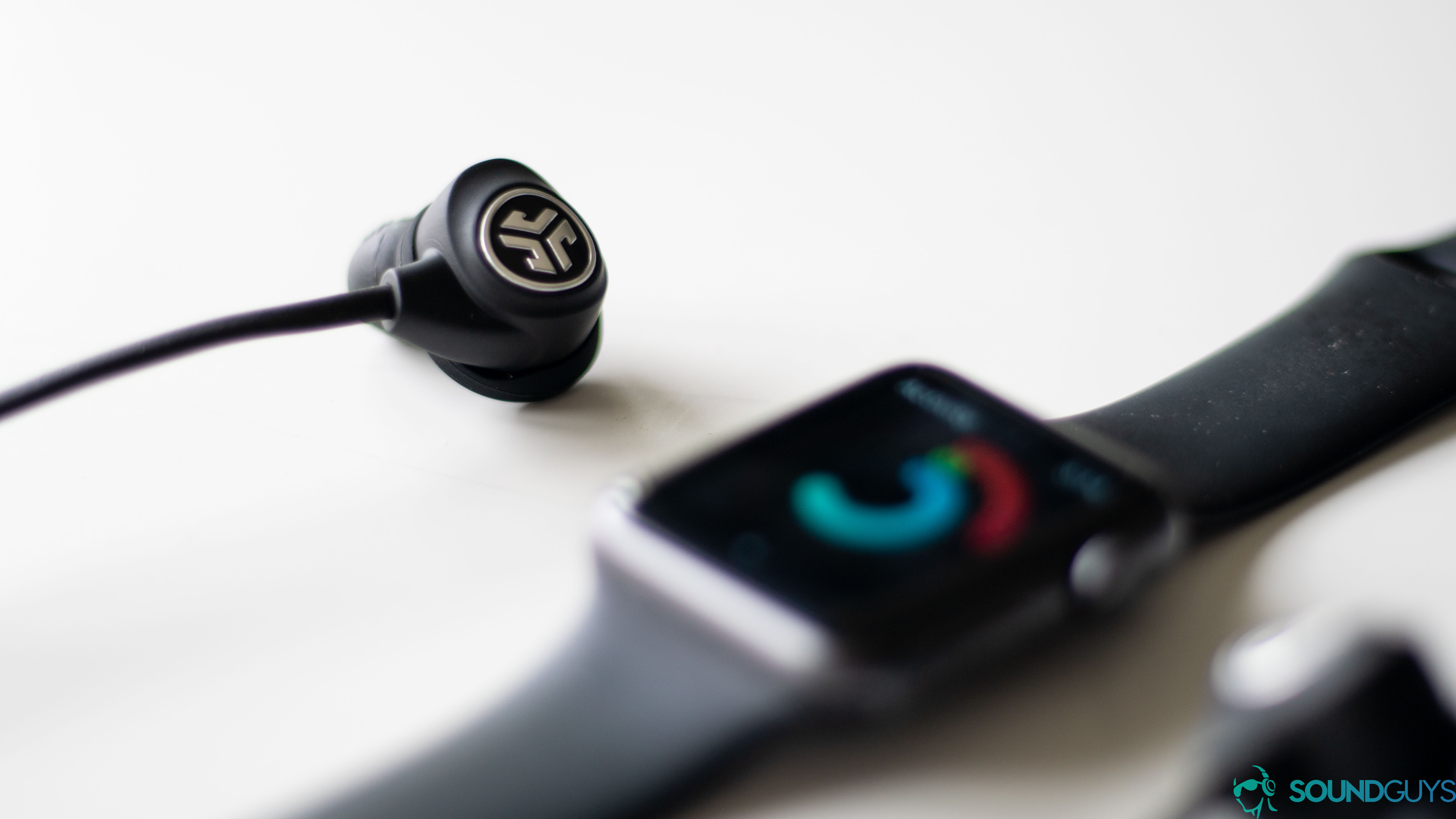 The headphones next to an Apple watch tracking fitness stats