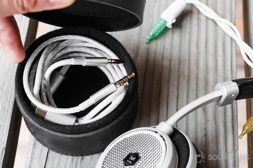 Master & Dynamic MW50 Wireless review: The USB-C and 3.5mm cables in the cyclindrical black leather cable box. The bottom right corner shows one of the earcups (outer side)
