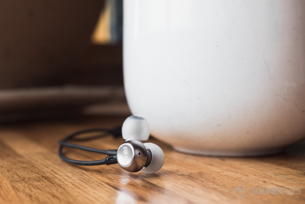 RHA MA390 review: The earbuds in front of a large, white coffe mug on a wooden surface.