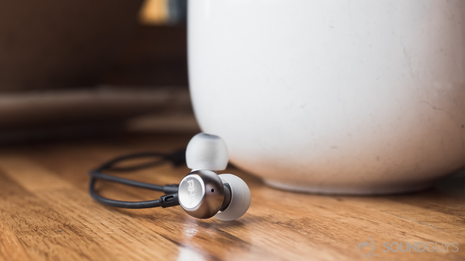 RHA MA390 review: The earbuds in front of a large, white coffe mug on a wooden surface.