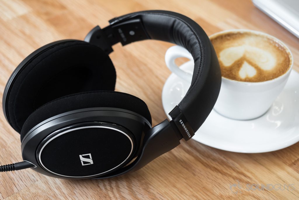 The headphones leaning against a cappuccino on a light-colored wood table.