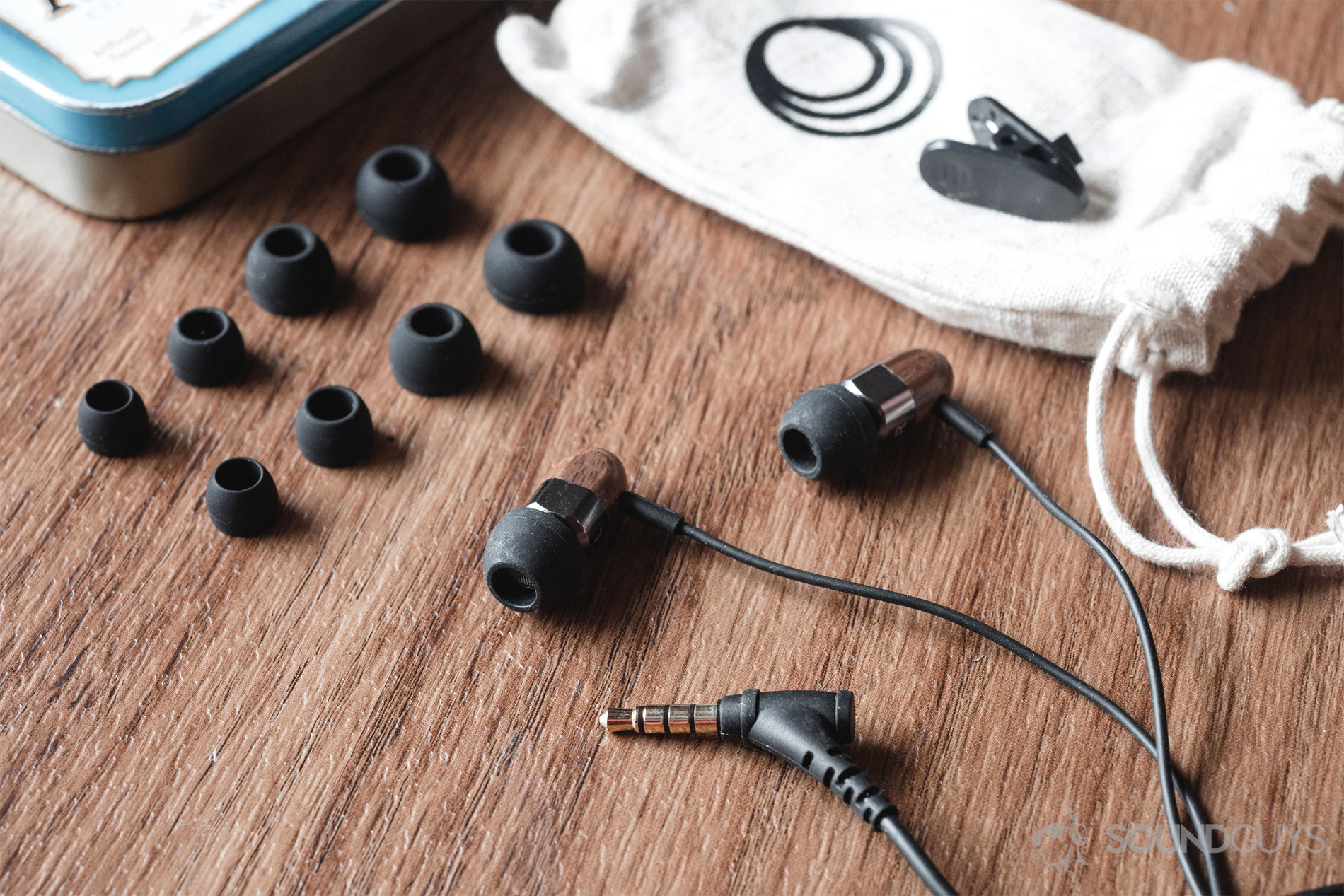 Thinksound ts03+mic review: A layout of all that's included with the 'buds. S/M/L/XL ear tips, a shirt clip, the earbuds, and a cotton drawsting pouch. All on wood-laminate surface.