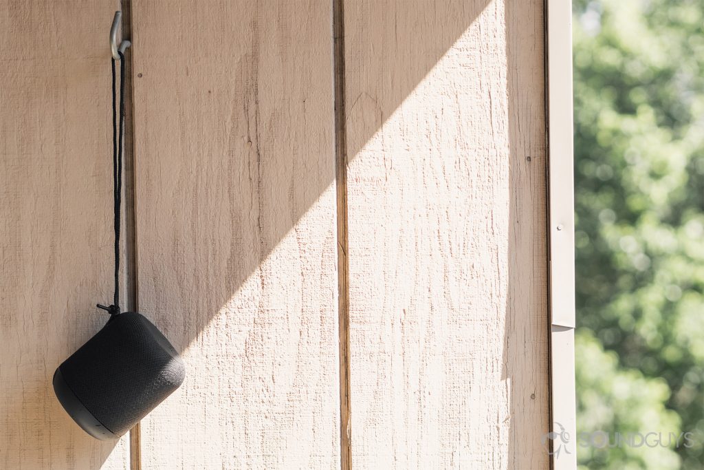 Anker Soundcore Motion Q review: The speaker is suspended from a hook protruding from a wood-paneled wall. The vertical right-quarter of the image consists of out of focus trees.