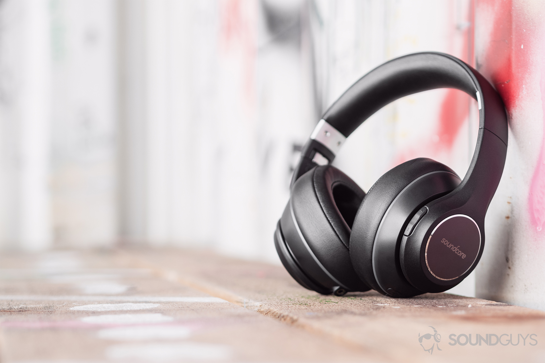 Anker_Soundcore Vortex_LK_8 Anker Soundcore Vortex review: The headphones resting on a wood bench, leaning against a graffiti'd and corrugated background.